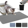 A gray and white cat is sitting on a gray silicone litter mat, with a black container of litter visible nearby.