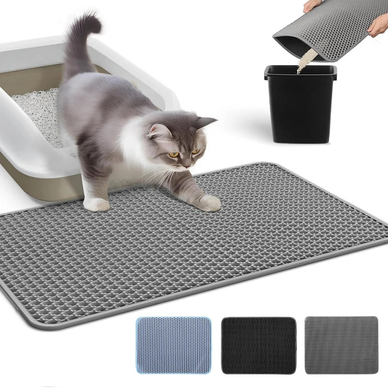 A gray and white cat is sitting on a gray silicone litter mat, with a black container of litter visible nearby.