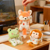 A hand is holding an orange fox plush toy and a green monkey plush toy on a wooden desk.