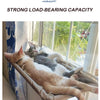 A tabby cat is relaxing in an aerial hammock pet bed near a window.