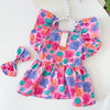 A pink and purple floral pet dress for a small dog with ruffled sleeves.