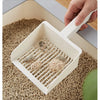 A hand is holding an extra-large white cat litter scoop with a hanging hook over a tray filled with cat litter.
