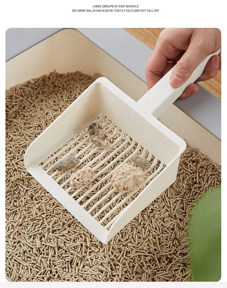 A hand is holding an extra-large white cat litter scoop with a hanging hook over a tray filled with cat litter.