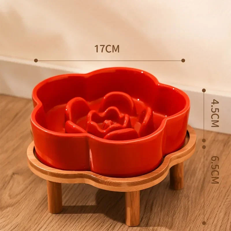 A bright red ceramic slow feeder cat bowl rests on a natural wooden stand.
