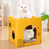 A fluffy white cat sits inside a yellow cardboard scratching box with an entrance hole.