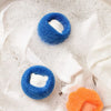 Three blue, white, and orange reusable pet hair and lint removal balls resting on a white cloth.