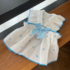 A white, textured dress with light blue polka dots and trim is displayed on a wooden surface.