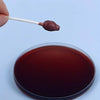 A dark reddish-brown substance is being placed onto a petri dish using a cotton swab for testing.