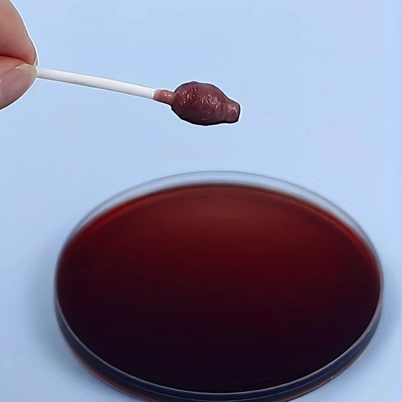 A dark reddish-brown substance is being placed onto a petri dish using a cotton swab for testing.