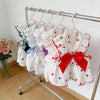 A display of white and pink breathable summer pet dresses with various patterns and a red bow hanging on a metal rack.