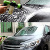 A hand sprays soapy foam onto a black car's windshield and body with a high-pressure cleaning gun.