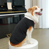A dog wearing a black tuxedo costume with a red bow tie, sitting on a white pedestal.