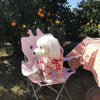 Un perro blanco y peludo vistiendo una sudadera de oso con estampado de corazón rosa, sentado en una silla de metal al aire l