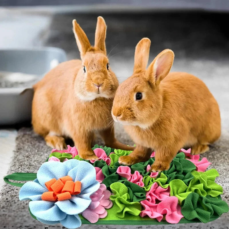 Two small brown rabbits standing on a green mat with pink and orange flowers