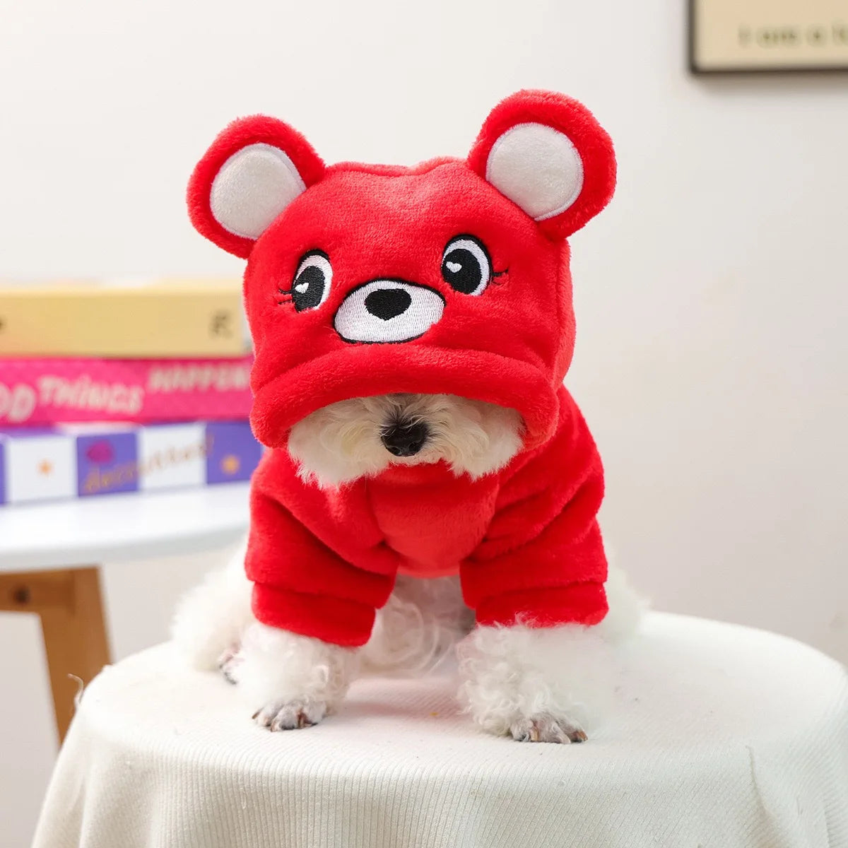 A red flannel hoodie with white trim and bear ears is shown on a white table.