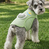 A gray dog wearing a light green cooling vest with a built-in fan, lying on green grass.
