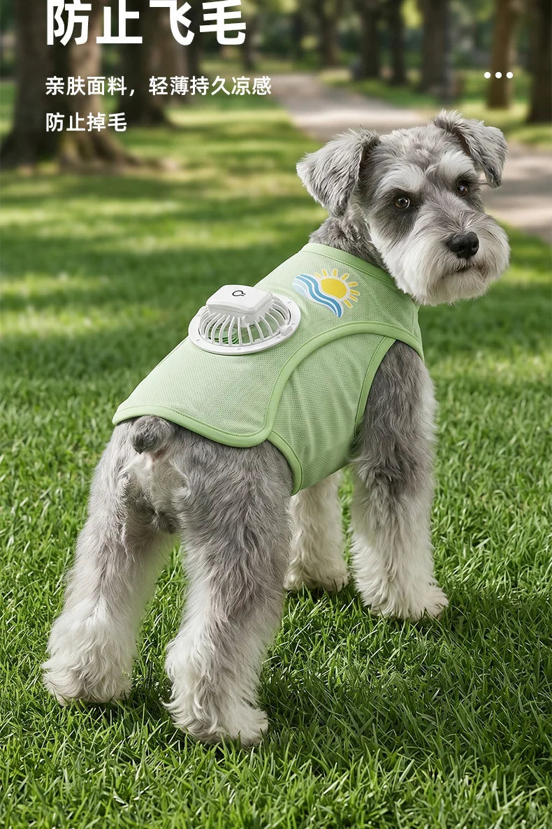 A gray dog wearing a light green cooling vest with a built-in fan, lying on green grass.