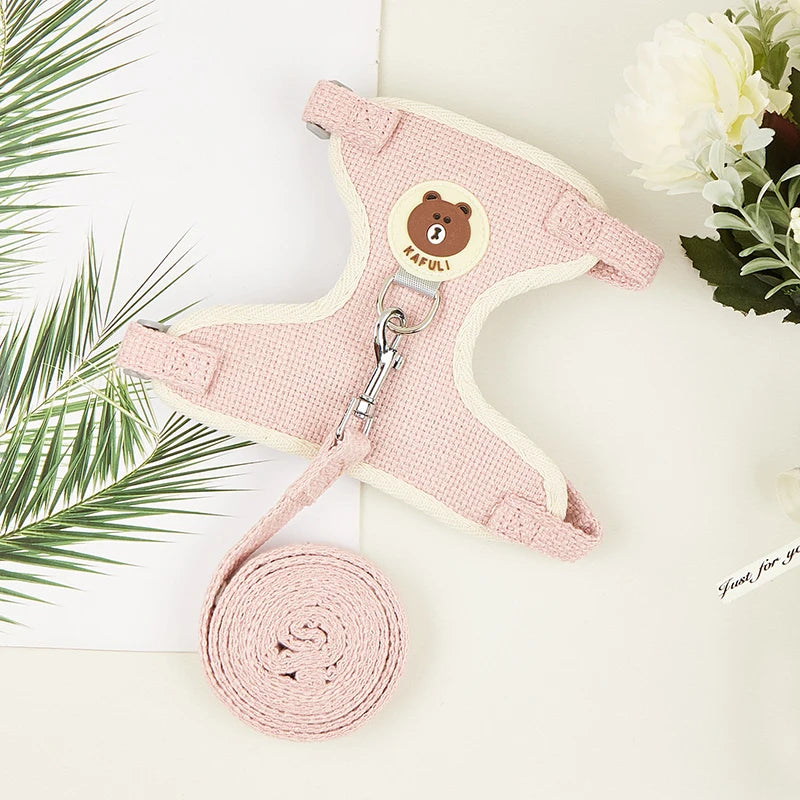 A pink padded rabbit harness and leash set with a round brown bear tag and coiled pink leash.
