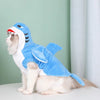 Un chat blanc portant un costume de requin bleu, assis sur une surface blanche devant un mur vert clair.