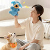 A woman is holding a blue plush toy while sitting on the floor with a dog nearby.