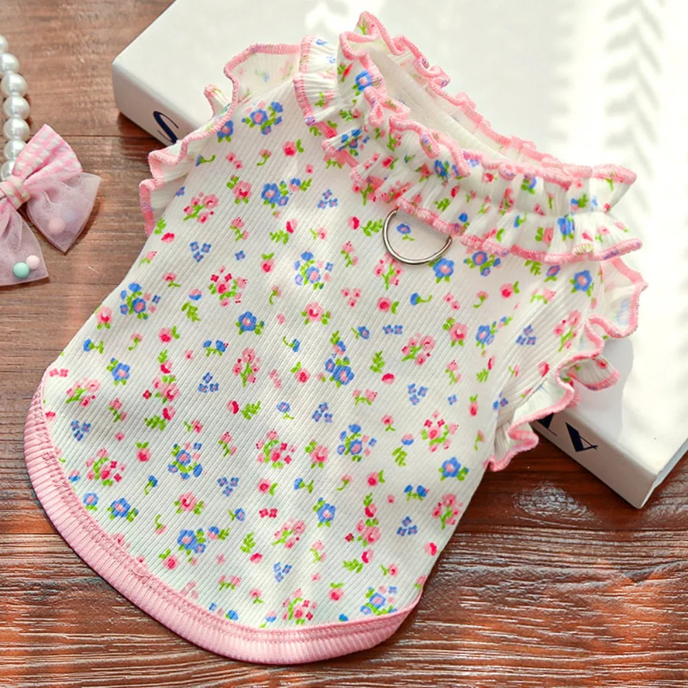 A pink floral princess pet dress for dogs and cats with ruffled trim lying on a wooden surface.
