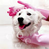 A white dog is wearing bright pink silicone grooming gloves for bathing or hair removal.