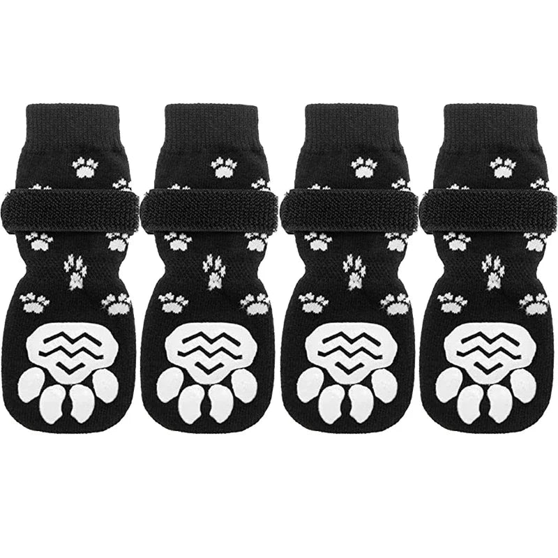 Four pairs of black anti-slip dog socks with traction straps featuring white paw prints