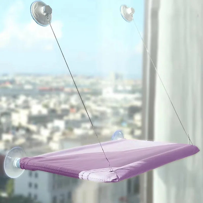 A purple hammock bed suspended by thin lines, featuring suction cup attachments for a cat window.
