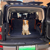 A golden retriever sits inside the open cargo area of a black SUV with an orange pet seat cover installed.