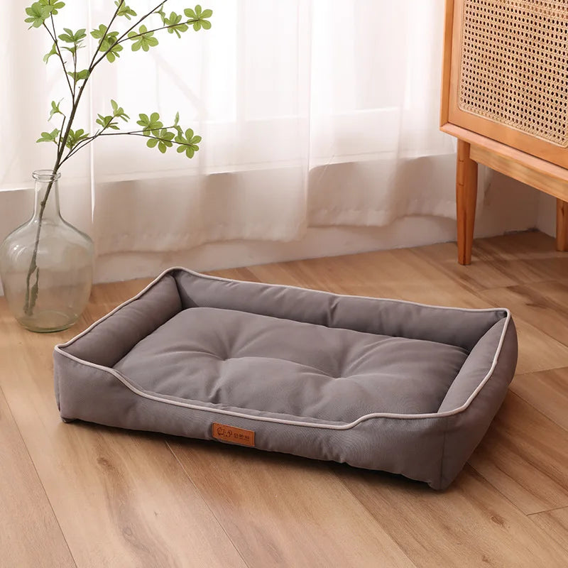 A gray corduroy pet sofa bed for dogs and cats resting on a wooden floor next to a window.