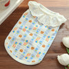 A white cotton dog vest with a lace collar and an orange cartoon print lying on a wooden surface.