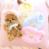 A pink plush pet sweater with yellow and blue accents, featuring a small brown puppy inside.