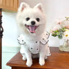 A fluffy white dog wearing a summer bow print pet dress sitting on a wooden surface.