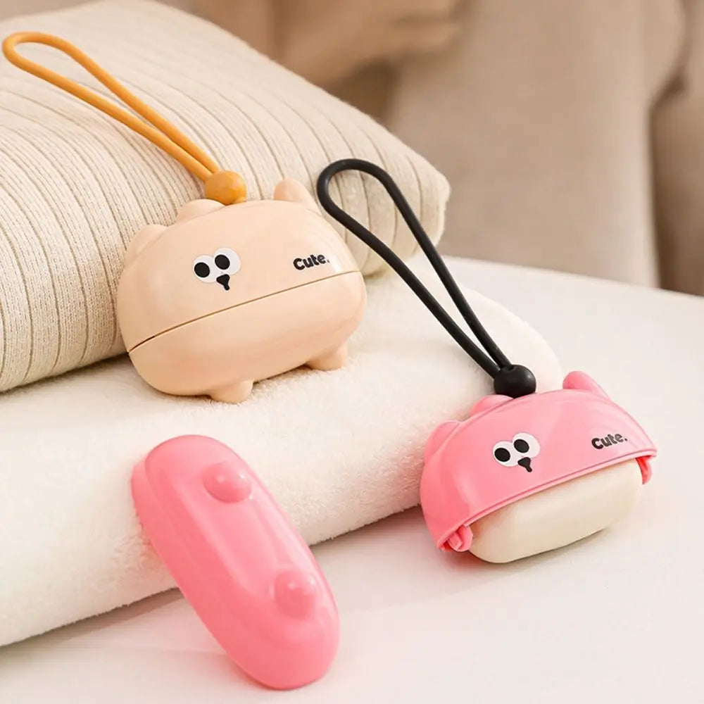 A pink reusable pet hair roller with a cute cartoon design is shown resting on a white towel.