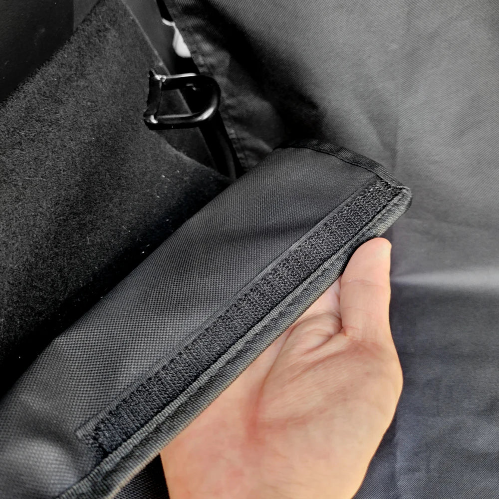 A hand is holding a black waterproof dog car seat cover fabric inside a dark car seat.