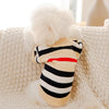 A beige striped knit sweater with black stripes and a red accent is displayed on a cream knitted blanket.