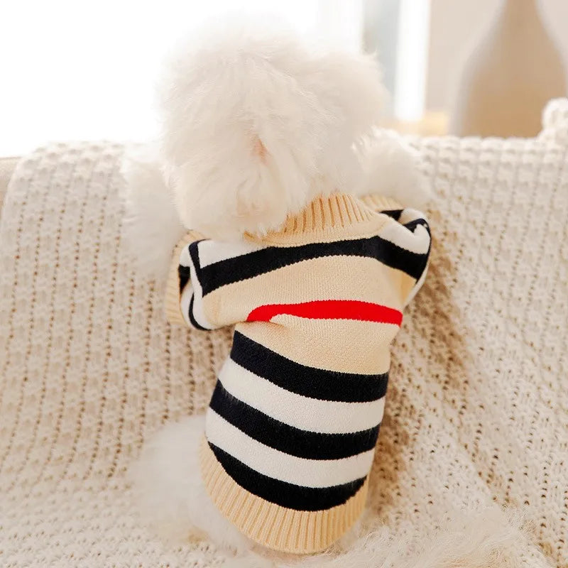 A beige striped knit sweater with black stripes and a red accent is displayed on a cream knitted blanket.