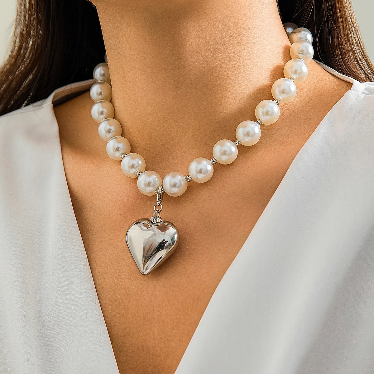 A close-up of a pearl choker necklace with a heart pendant worn against a light-colored garment.