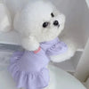 Poupée de chien blanche et duveteuse portant une robe violette à manches flottantes.