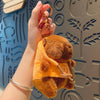 A hand is holding a brown capybara plush doll wearing an orange hoodie and a gold-colored necklace.