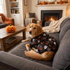 A golden retriever wearing a black and orange Halloween costume pajama is relaxing on a gray sofa.