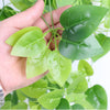 A hand holds a branch of artificial green ivy vine with glossy leaves.