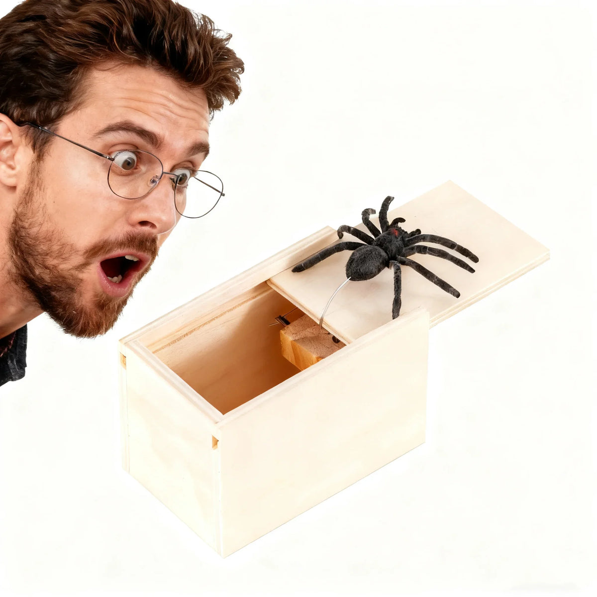 A man looks surprised while holding an open wooden box containing a black spider.