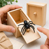 A hand is opening a wooden box to reveal a black spider inside.