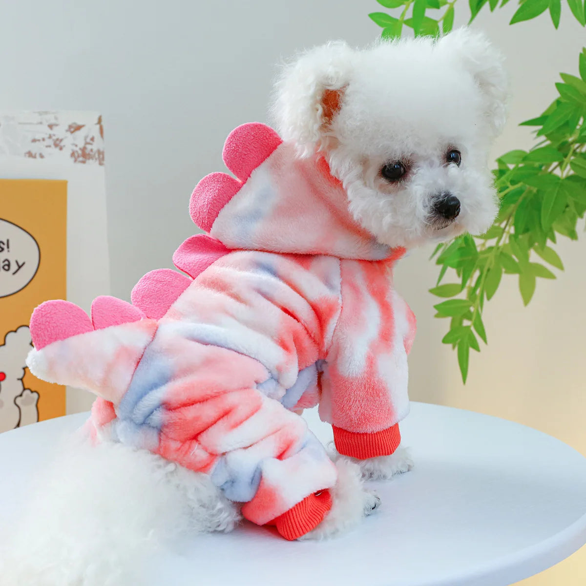 A fluffy white dog wearing pink and blue patterned fleece overalls.