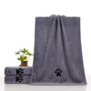 Serviette de bain pour animaux gris foncé ultra-absorbante avec motif empreinte de patte, à côté d'une petite plante en pot.