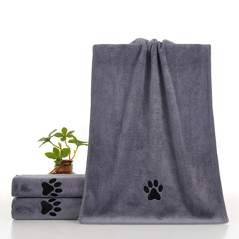 Serviette de bain pour animaux gris foncé ultra-absorbante avec motif empreinte de patte, à côté d'une petite plante en pot.