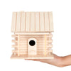 A light wood birdhouse with a pitched roof and a circular entrance is held in a hand.