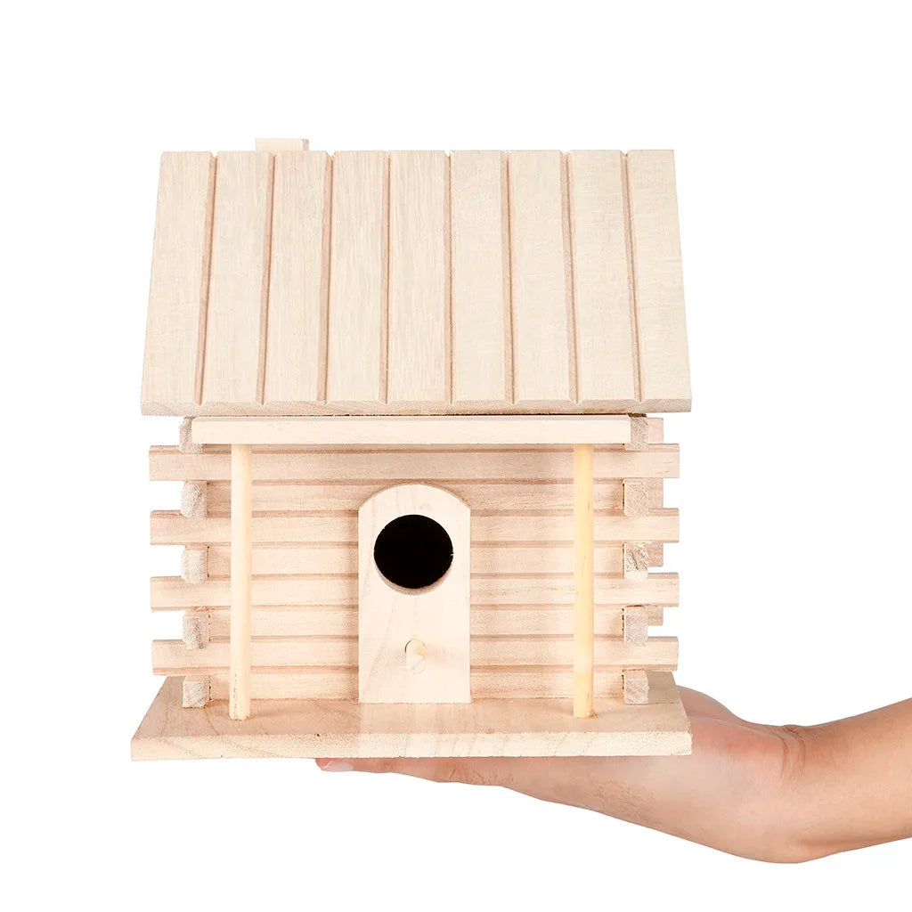 A light wood birdhouse with a pitched roof and a circular entrance is held in a hand.