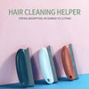 Three hair cleaning helper tools in dark blue, white, and brown resting on a blue surface.